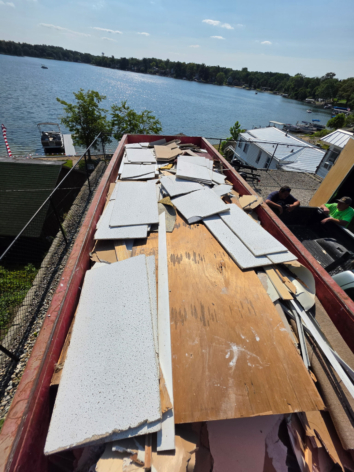 Roll-off dumpster loaded with drywall and construction debris overlooking Island Lake in Brighton, Michigan