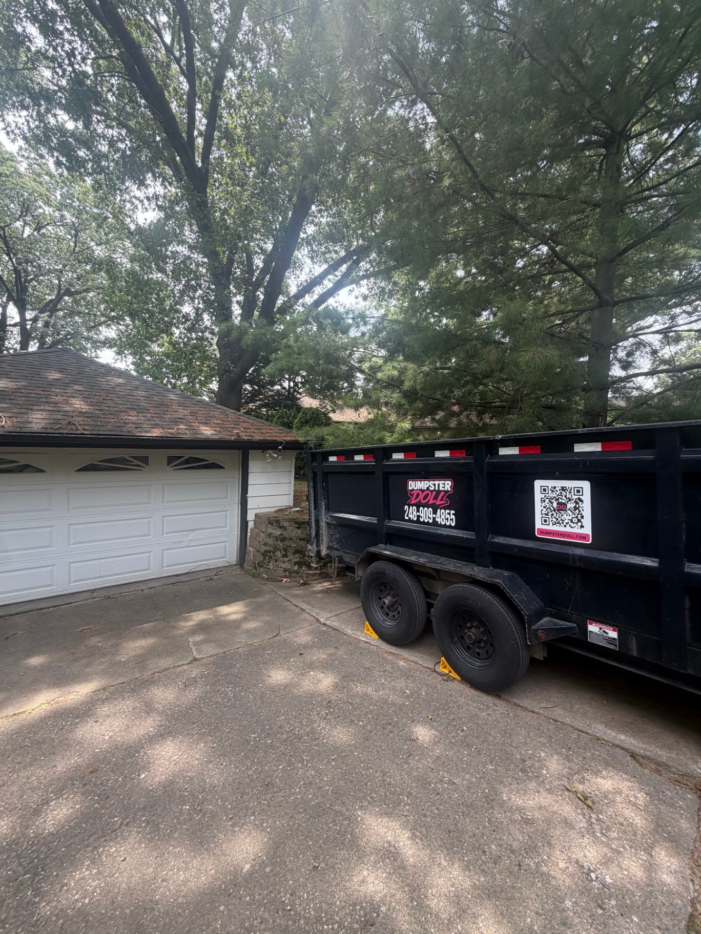 Dumpster Doll roll-off dump trailer parked in a wooded driveway for a home cleanout in Waterford, Michigan